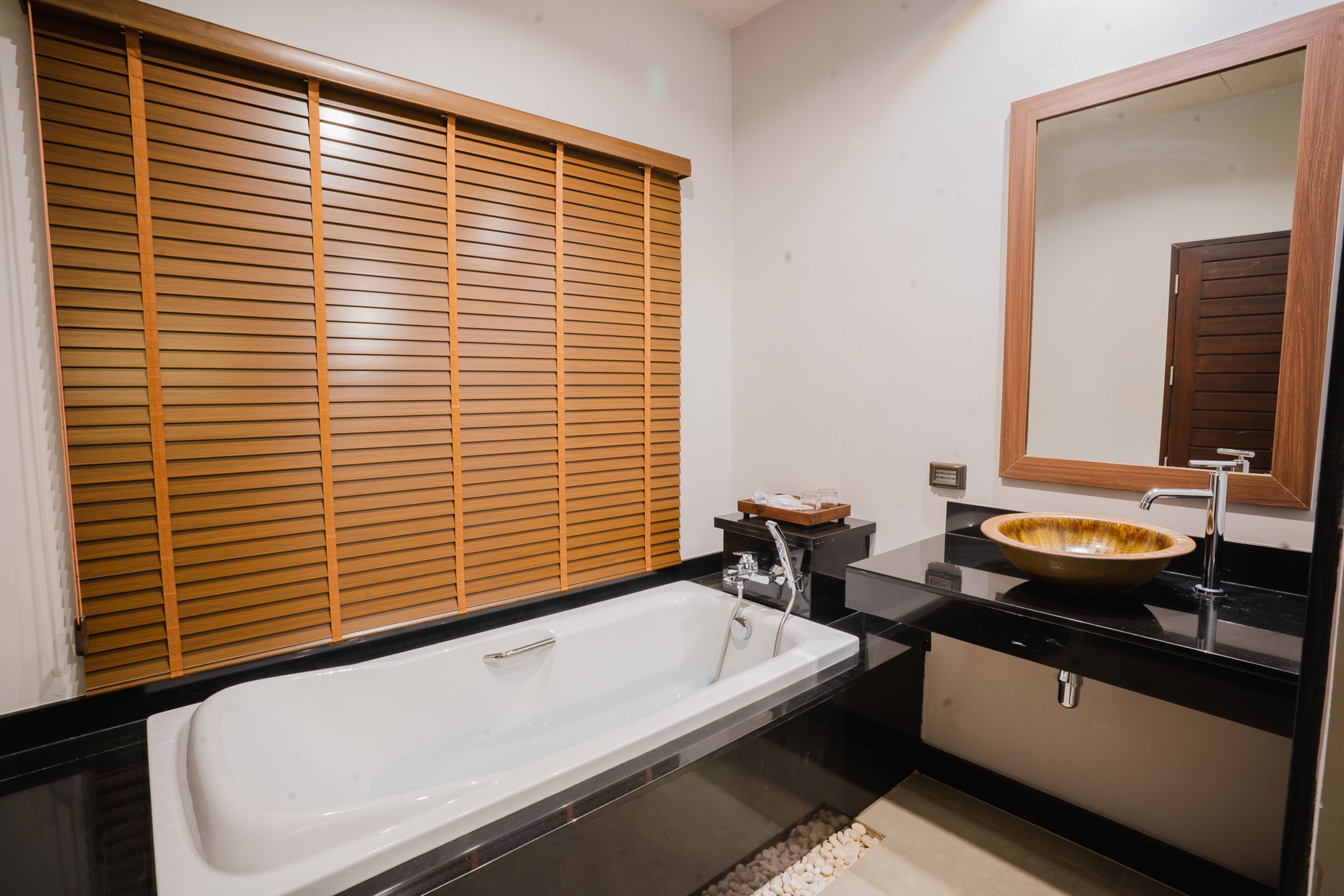 A modern bathroom with a bathtub, a wooden window blind, a sink with a bowl, and a mirror.