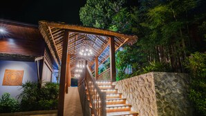 A staircase with wooden railings and stone walls, leading to a covered area with hanging lights. - Malabar  Pool Villa Phuket  (Ratsada)