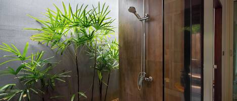 A modern bathroom with a glass shower enclosure, a wooden bench, and a row of green plants along the wall.