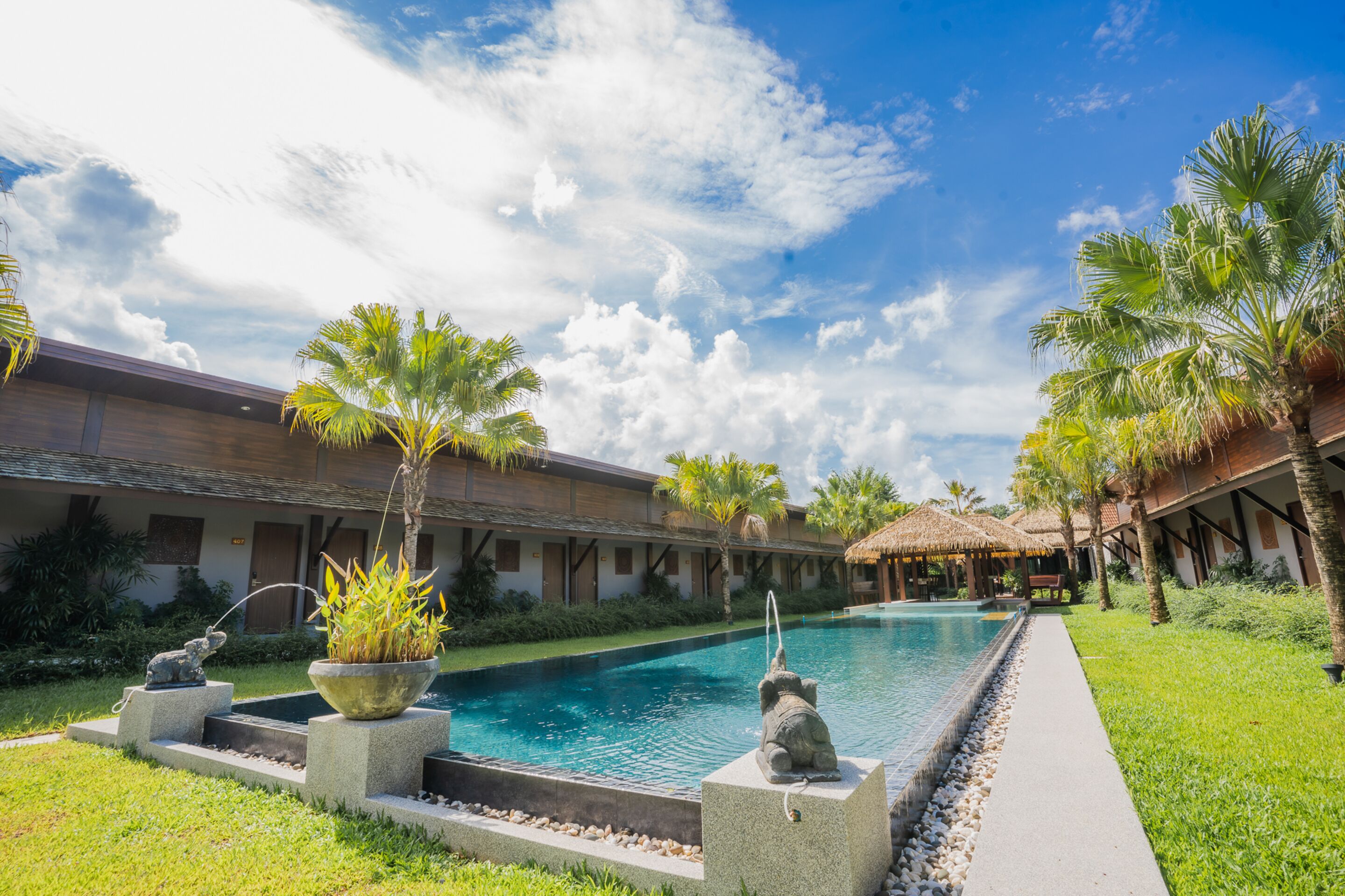 A pool area with a clear sky, palm trees, and a building with a thatched roof.