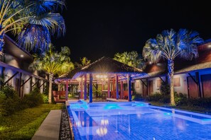 A nighttime view of a resort with a swimming pool, palm trees, and a covered seating area. - Malabar Pool Villa Phuket (Ratsada)