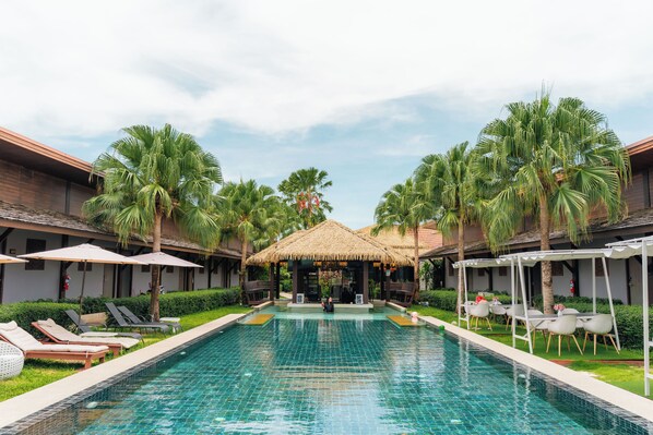 A swimming pool with lounge chairs and umbrellas, surrounded by palm trees and a thatched-roof structure. - Malabar Pool Villa Phuket (Ratsada)