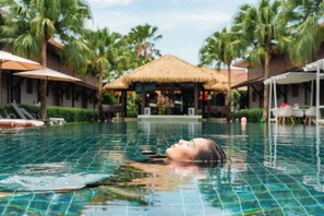A swimming pool with a person relaxing in it, surrounded by palm trees and thatched-roof structures. - Malabar  Pool Villa Phuket  (Ratsada)