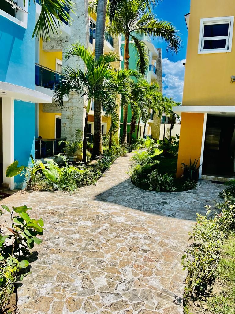 A courtyard with a stone pathway, surrounded by buildings with balconies and palm trees.