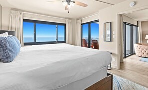 A bedroom with a large bed, a ceiling fan, and a view of the ocean through large windows.
