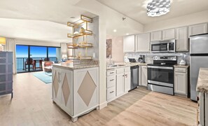 A modern kitchen with stainless steel appliances, a central island with a sink, and a view to the outside.
