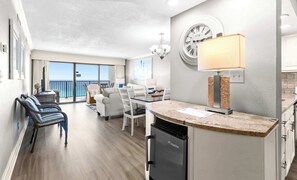 Cozinha moderna com lava-louças embutida, espaço de refeições com mesa e cadeiras, e vista para o oceano através de grandes janelas.