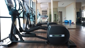 A gym with multiple treadmills and elliptical machines, a large mirror, and a wooden floor. - Hotel Osaka Pik2 (Kosambi)