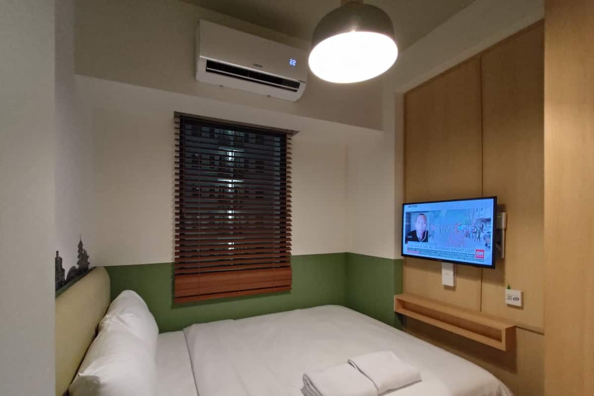A hotel room with a bed, a television mounted on the wall, and an air conditioning unit above the bed.
