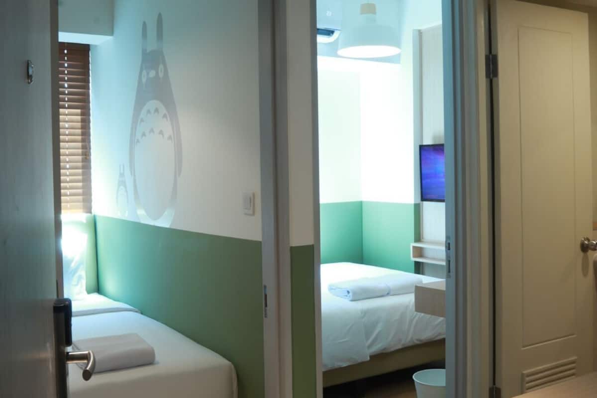 A hotel room with two beds, a small table, a TV, and a bathroom.