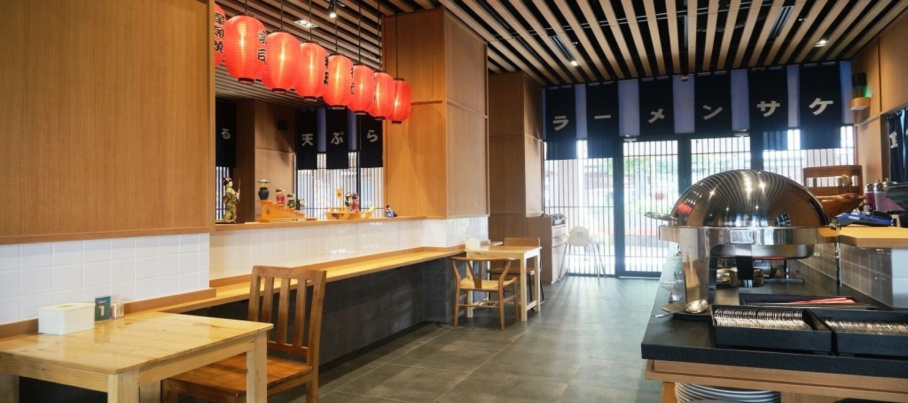 Interno di un ristorante con arredi in legno, una macchina da caffè e lanterne rosse.