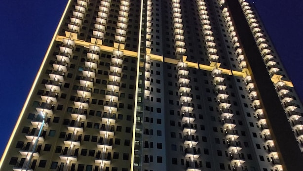A high-rise hotel with multiple balconies, a well-lit entrance, and a parking area with cars. - Hotel Osaka Pik2 (Kosambi)