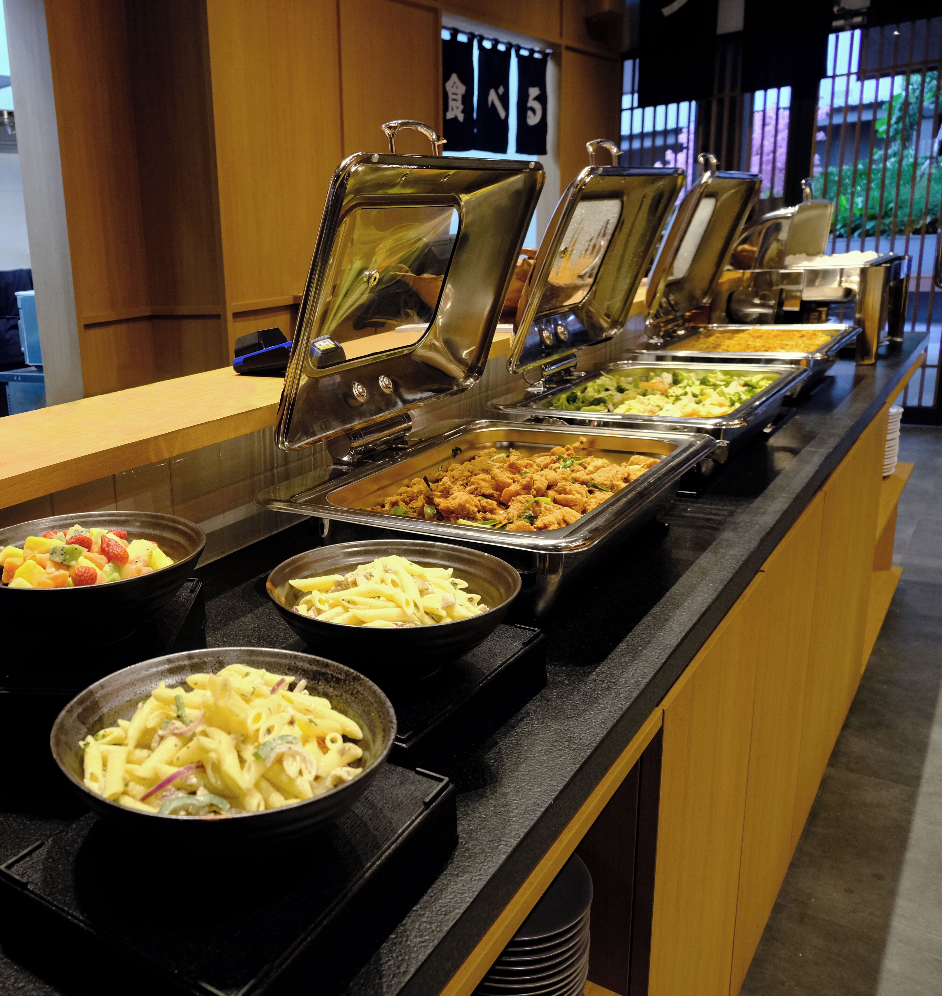 A buffet line with various food options, including pasta, salads, and other dishes.