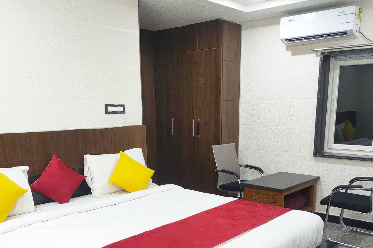 A hotel room with a large bed, a desk, a chair, a wardrobe, and an air conditioning unit.