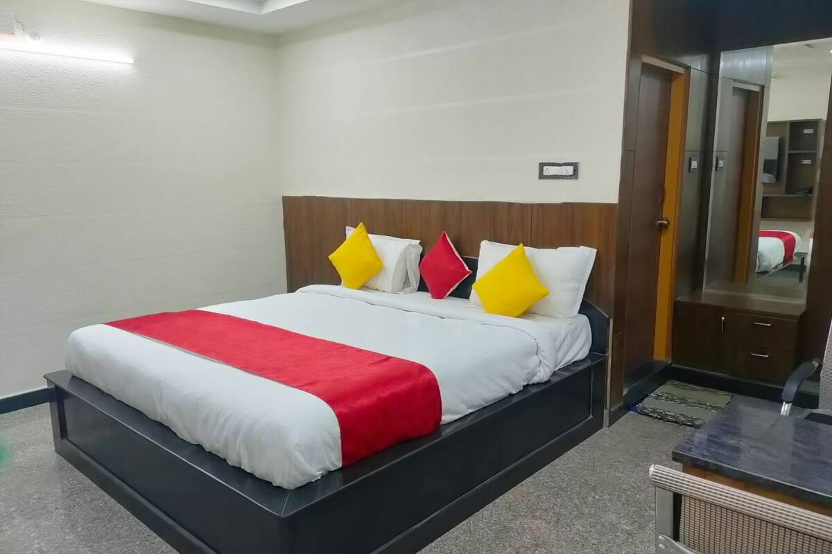 A hotel room with a bed, a wooden headboard, a small table, and a mirror.