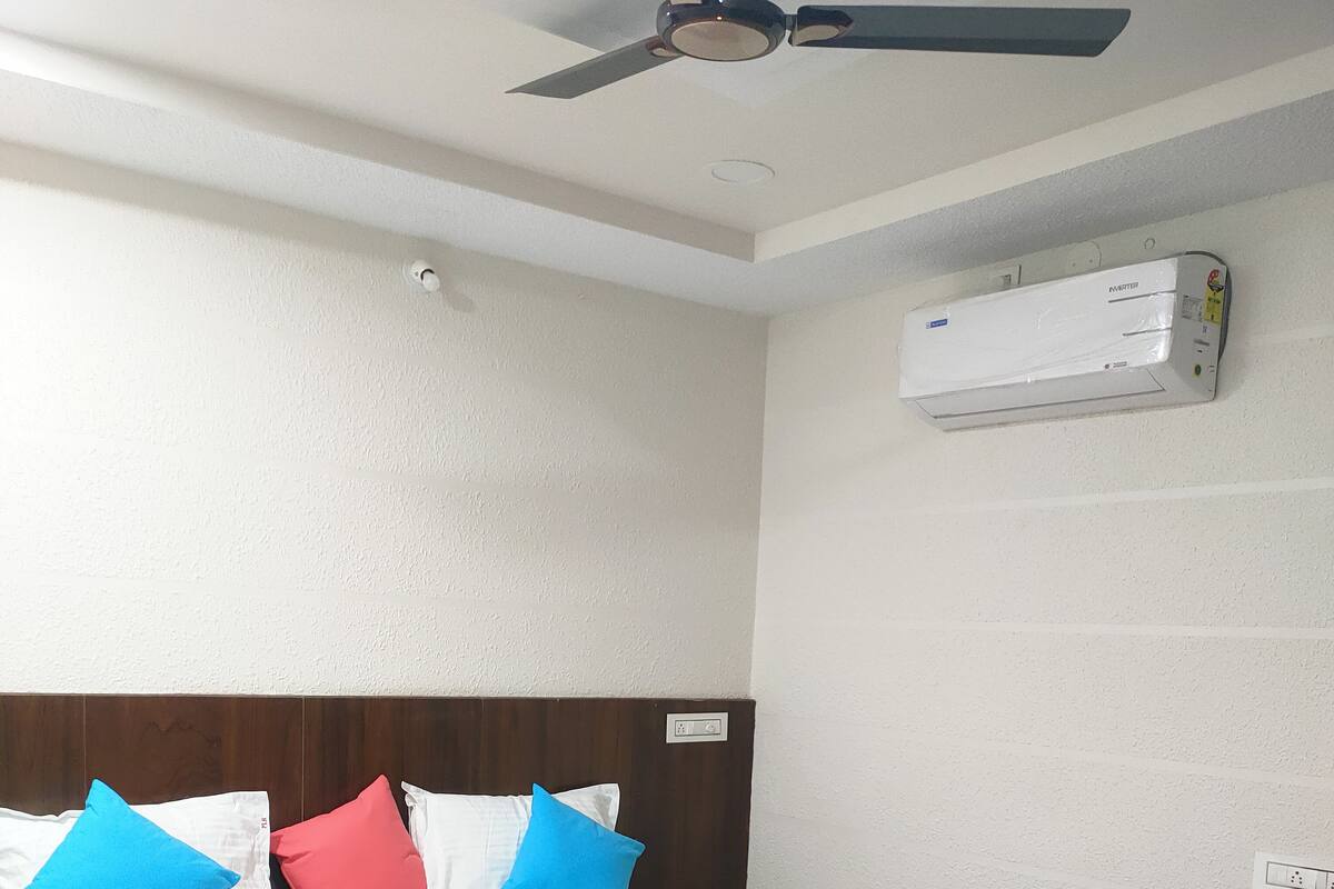 A hotel room with a bed, a ceiling fan, an air conditioning unit, and a desk with a chair.