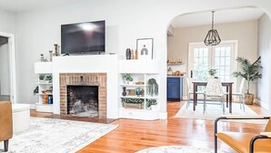 Ein Wohnzimmer mit Kamin, einem darüber montierten Fernseher und einem Essbereich mit Tisch und Stühlen.