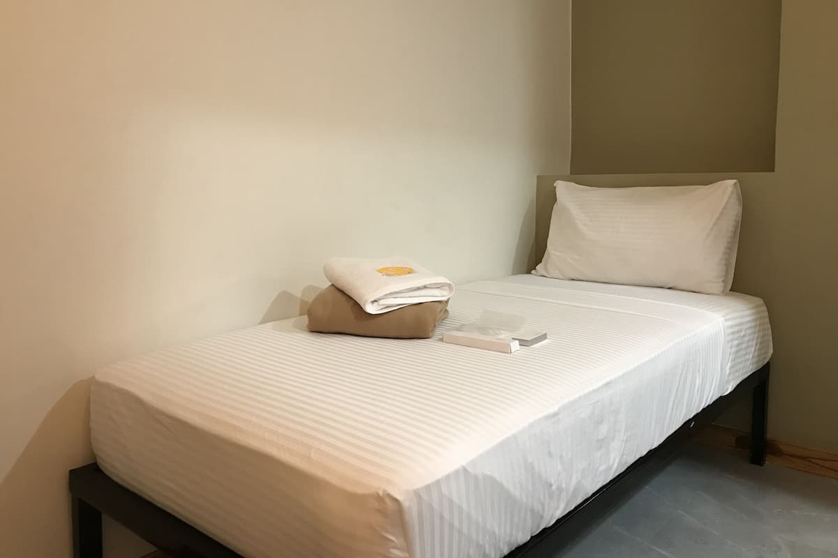 Un lit simple avec un matelas blanc et un oreiller beige, une serviette pliée et une télécommande posées sur le lit.