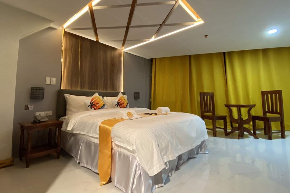 Une chambre d’hôtel moderne avec un grand lit, une tête de lit en bois et un luminaire au plafond aux motifs géométriques.