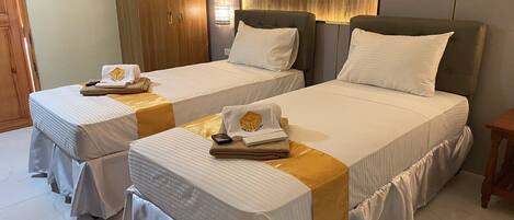 A hotel room with two single beds, each with a white bedspread and a gold accent. There are wooden wardrobes and a small wooden table.