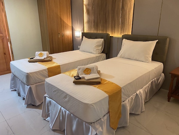 A hotel room with two single beds, each with a white bedspread and a gold accent. There are wooden wardrobes and a small wooden table. - NGN GRAN HOTEL (Tuguegarao)