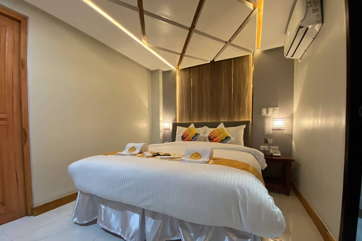 Une chambre d’hôtel moderne dotée d’un grand lit, de tables de chevet, d’un appareil de climatisation et d’une porte en bois.