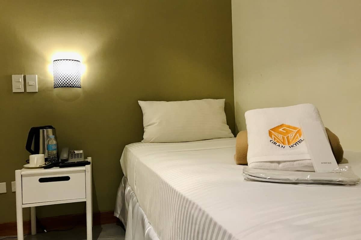 Une chambre d’hôtel avec un lit, une table de chevet, une lampe et un kit de bienvenue posé sur le lit.