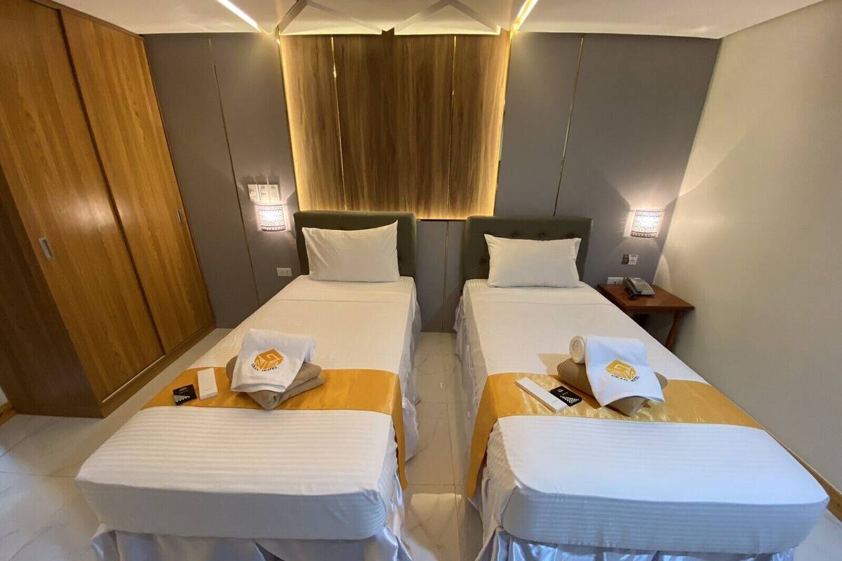 Une chambre d’hôtel avec deux lits, une armoire en bois, des lampes de chevet et une petite table avec un téléphone et une télécommande.