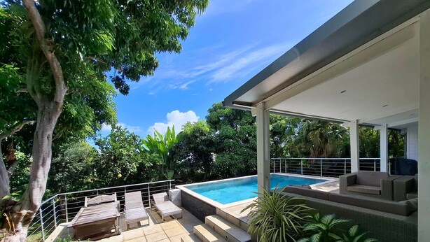 Un área de piscina moderna al aire libre con una zona de estar cubierta y escalones que dan a la piscina.