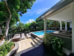 Un espace piscine extérieur moderne, doté d’un coin salon couvert et de marches menant à la piscine.