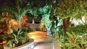 Un sendero nocturno bordeado por exuberante vegetación y muros de piedra, que lleva a un edificio de piedra.