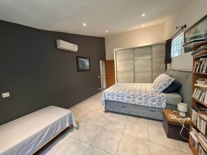 Une chambre à coucher comprenant un lit, une table de chevet, une bibliothèque, un climatiseur fixé au mur et un tableau encadré.