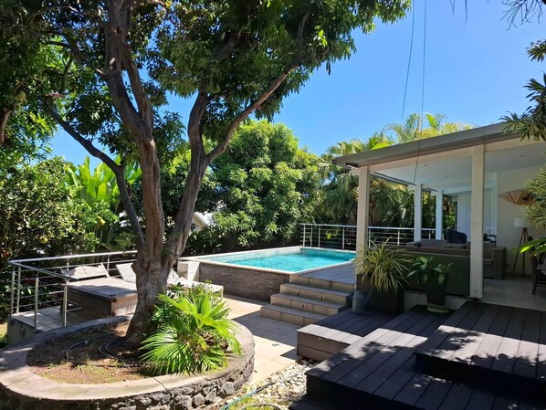 Une piscine dotée d’un patio couvert, entourée d’une végétation luxuriante et d’arbres.