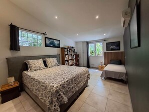 Une chambre avec un grand lit, un plus petit lit, une bibliothèque et une fenêtre avec des rideaux.