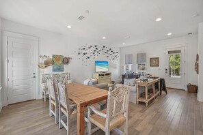 A spacious dining area with a wooden table and white chairs, a television, and a wall decorated with abstract art.