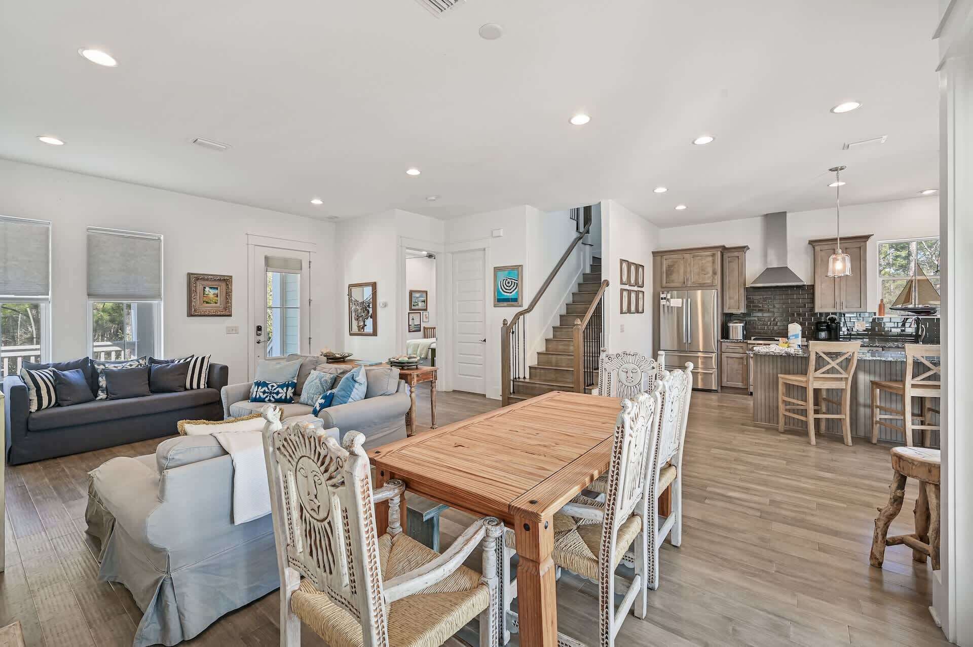 A spacious living area with a wooden dining table, a staircase leading to a kitchen, and a large window providing natural light.