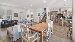 Un vaste espace de vie comprenant une table à manger en bois, un escalier menant à la cuisine et une grande fenêtre laissant entrer la lumière naturelle.