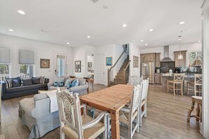 Un vaste espace de vie comprenant une table à manger en bois, un escalier menant à la cuisine et une grande fenêtre laissant entrer la lumière naturelle.