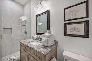 A bathroom with a granite countertop, a large mirror, and two framed wall art pieces.
