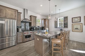 A modern kitchen with stainless steel appliances, a central island, wooden chairs, and pendant lighting.