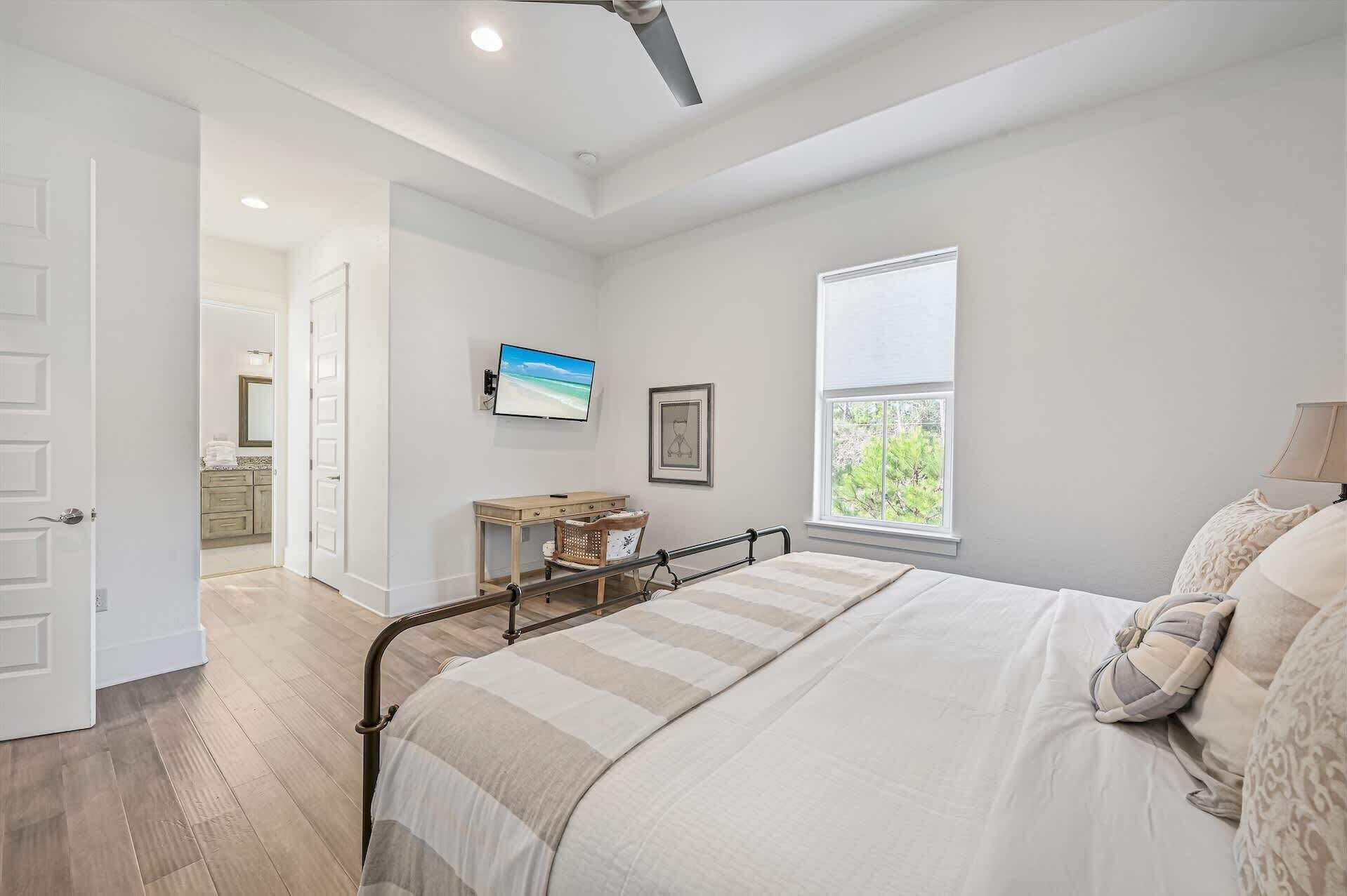A bedroom with a bed, a bedside table, a window, and a door leading to a bathroom.