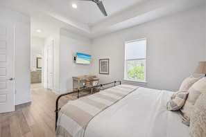 A bedroom with a bed, a bedside table, a window, and a door leading to a bathroom.
