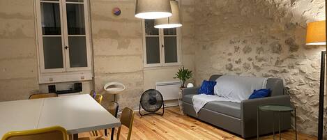 A room with a dining table, chairs, a sofa, a fan, and a lamp.