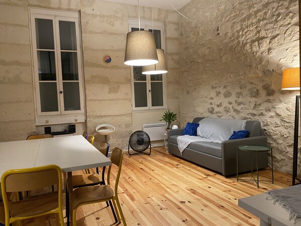 A room with a dining table, chairs, a sofa, a fan, and a lamp.