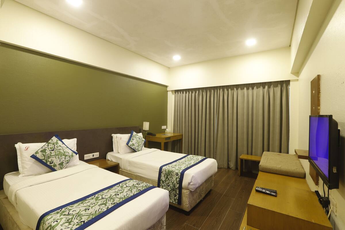 A hotel room with two beds, a TV, a desk, and a window with curtains.