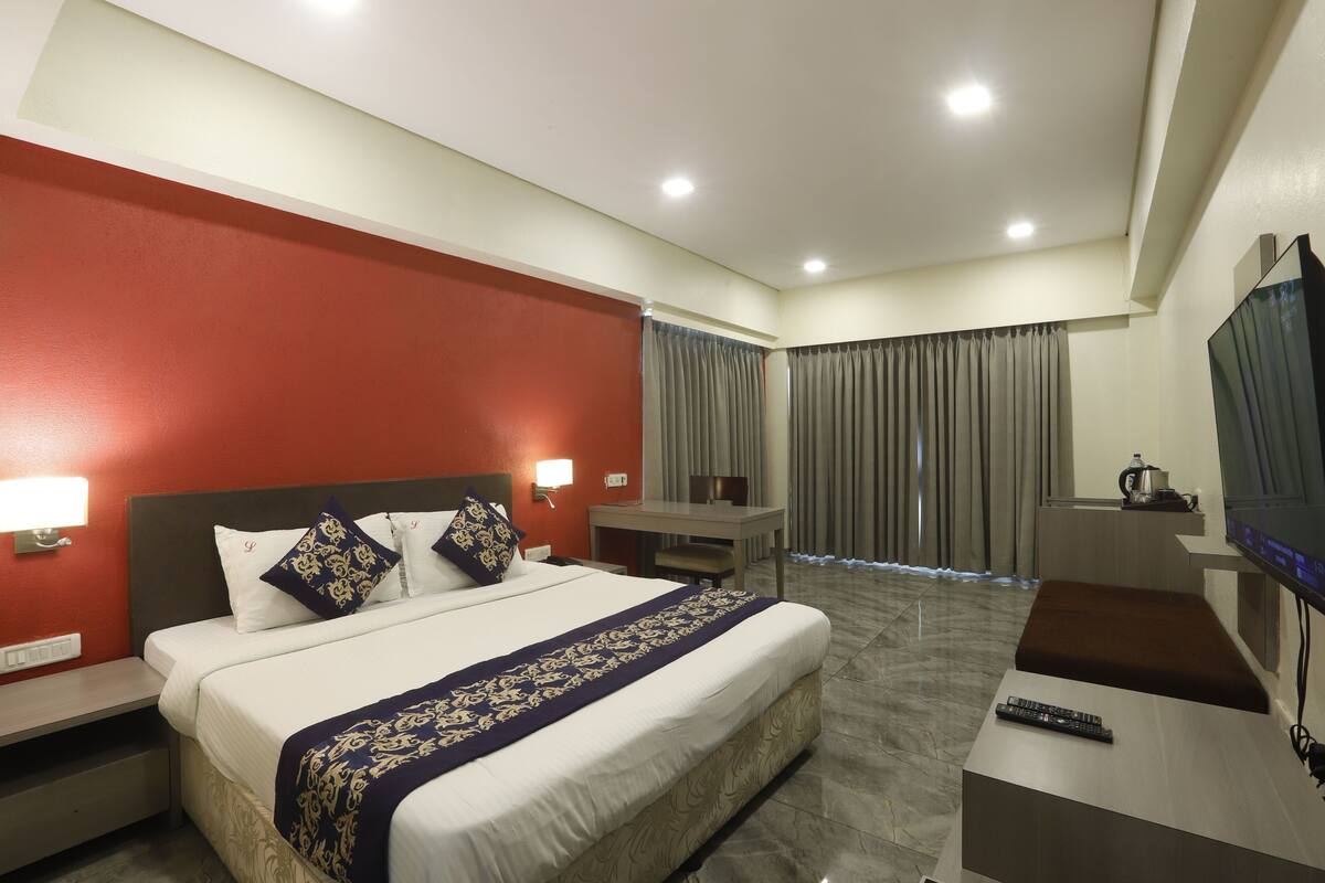 A hotel room with a large bed, a desk, a TV, and a view of the outdoors.
