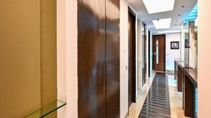 Un couloir d’hôtel moderne avec une rambarde en verre, des portes en bois et un sol à motifs.
