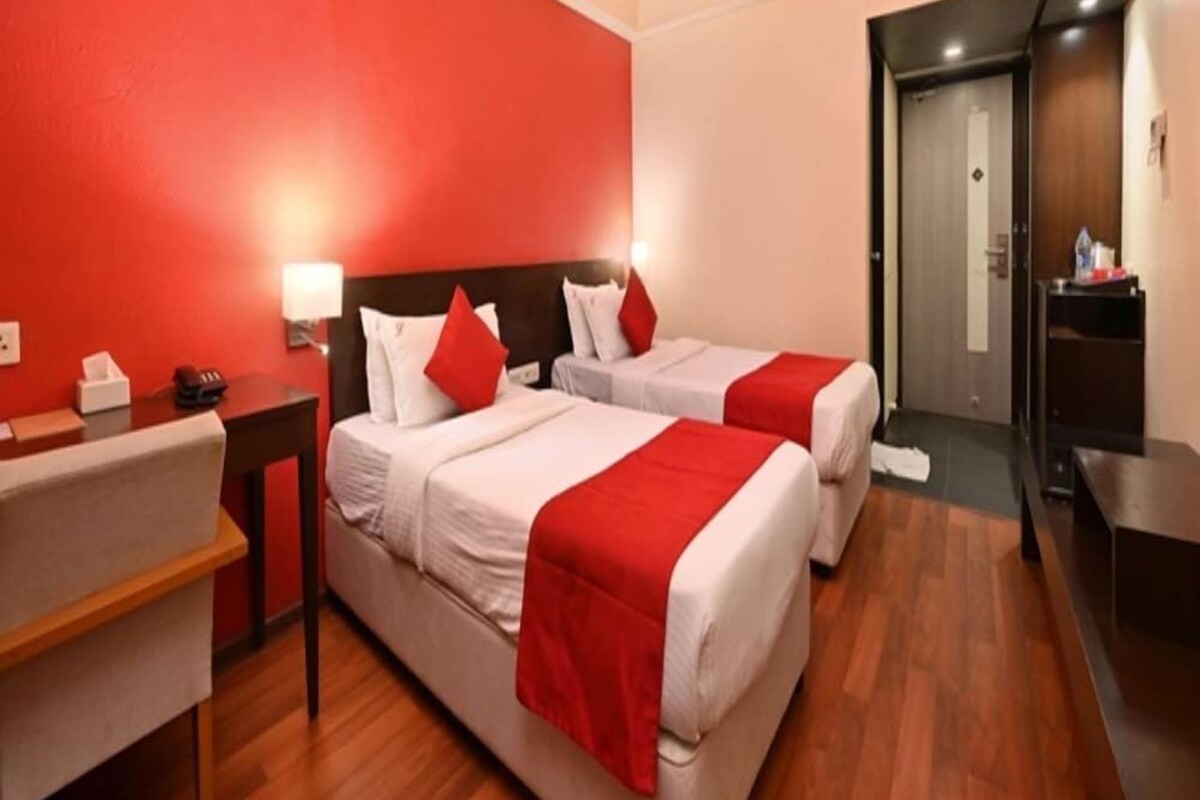 A hotel room with two beds, a desk, and a mirror.