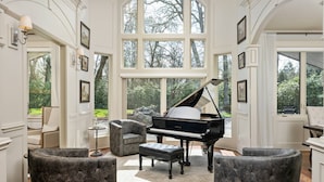A grand piano in a spacious room with large windows, elegant chairs, and framed artwork on the walls. - Country Luxury in Manor, Pet Friendly, Hot Tub, Indoor Basketball Ct, Billiards, on 2 Acres (Newberg)
