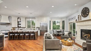 A spacious living room with a fireplace, a kitchen with a large island, and a dining area with a view of the outdoors. - Country Luxury in Manor, Pet Friendly, Hot Tub, Indoor Basketball Ct, Billiards, on 2 Acres (Newberg)